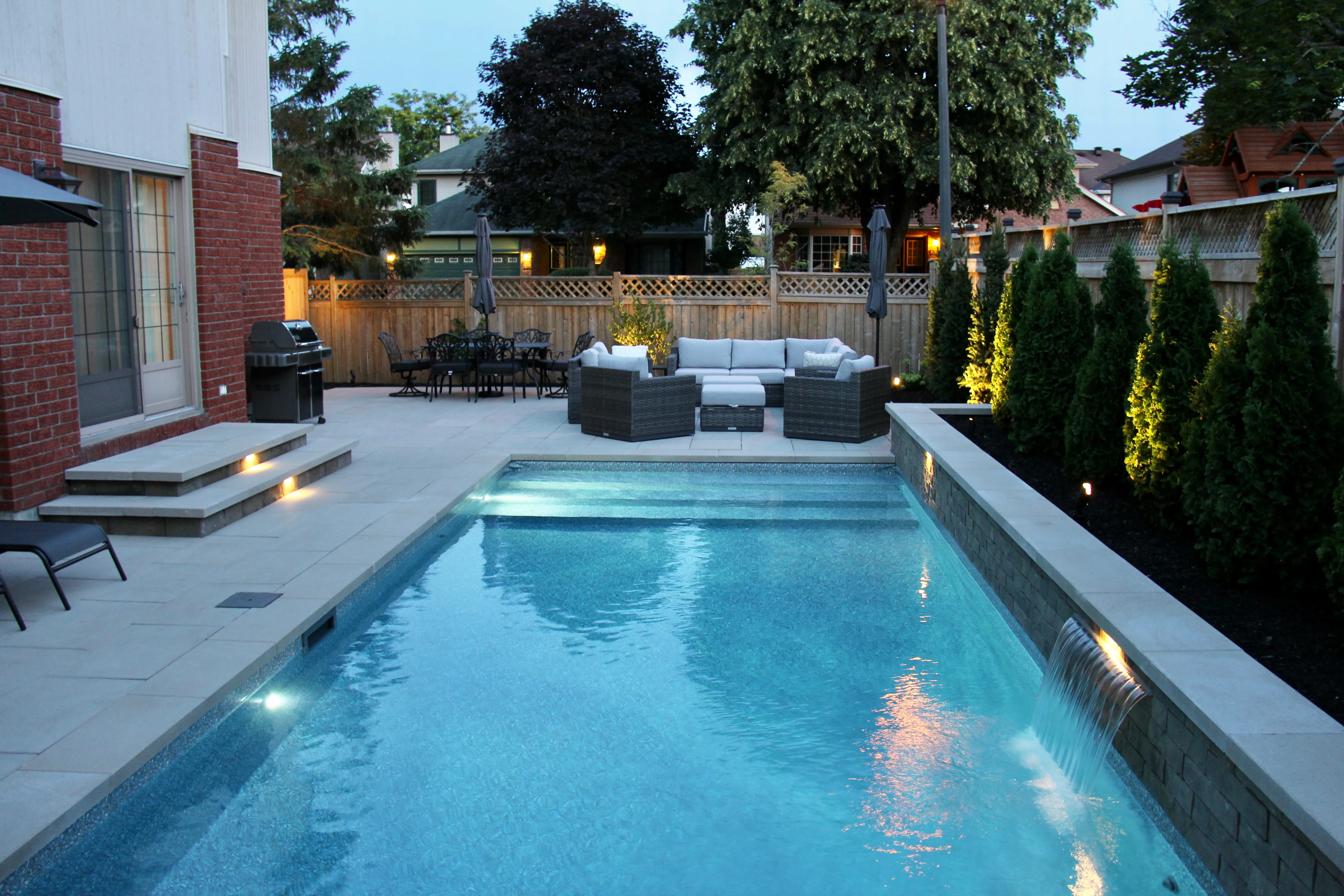 Illuminated inground pool and backyard at blue hour