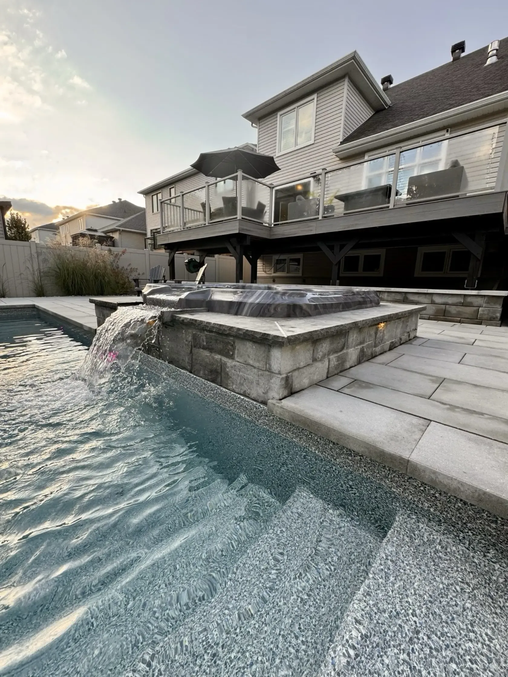 Hot tub with a custom stone surround spilling into the pool at dusk