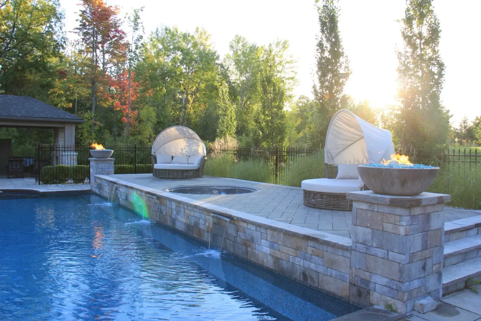 Sunset over the pool with a lit fire bowl and twin sheer-descent waterfalls