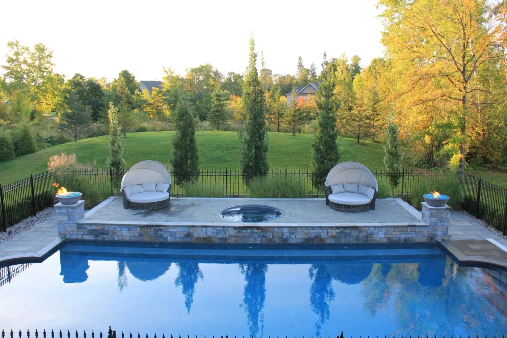 Wide pool vista with symmetric daybeds, fire bowls and fall colour