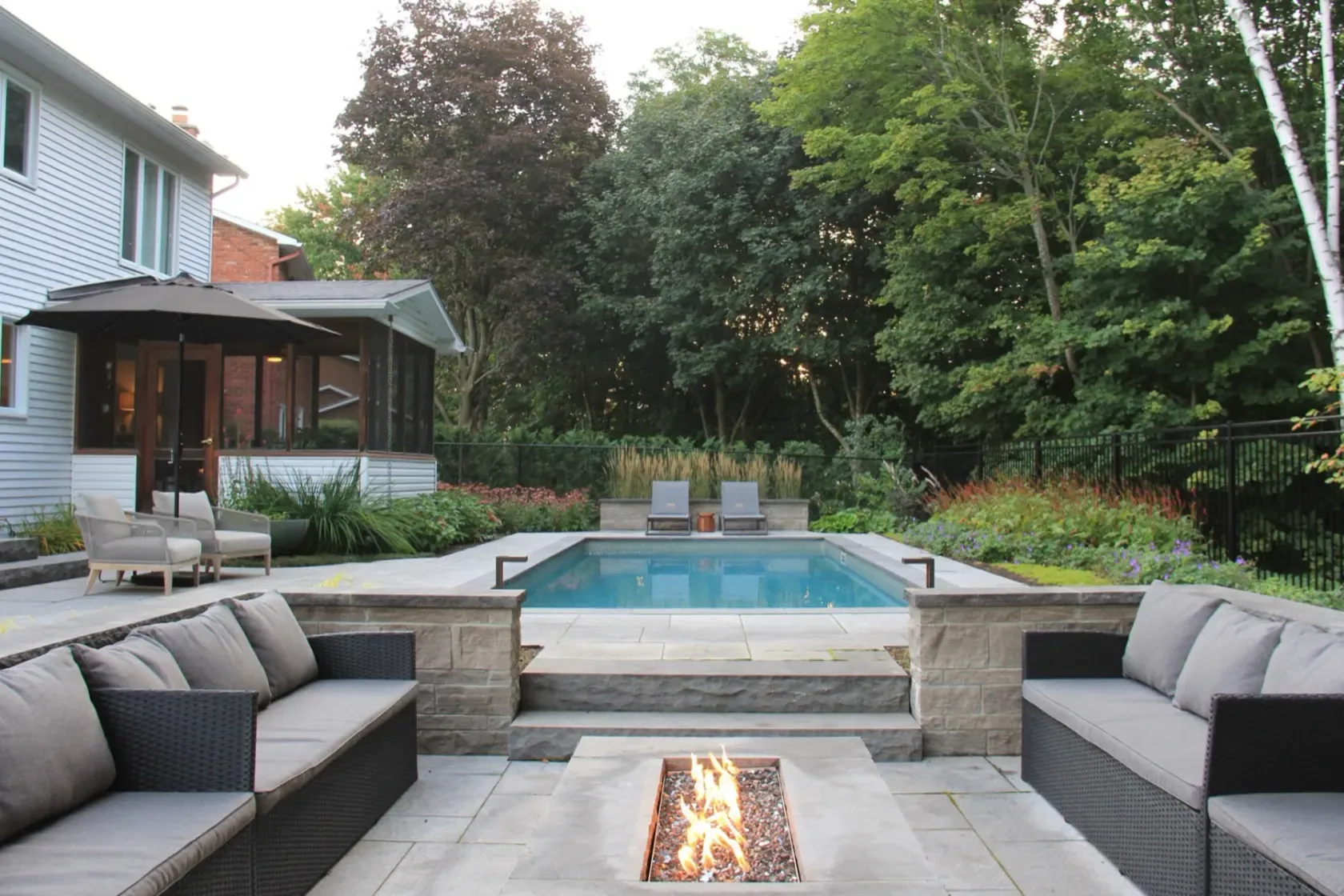 Linear pool behind a sunken outdoor lounge at blue hour
