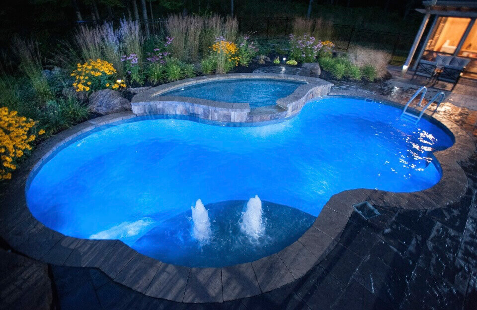 kidney bean shaped inground pool with attached hot tub spa and led lighting throughout