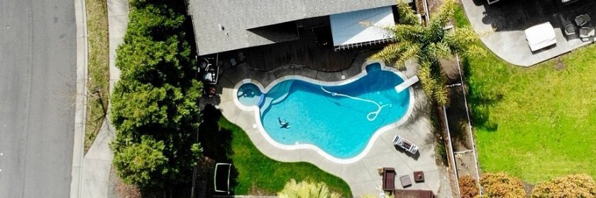 Aerial view of a home and backyard with a large pool and tropical trees.