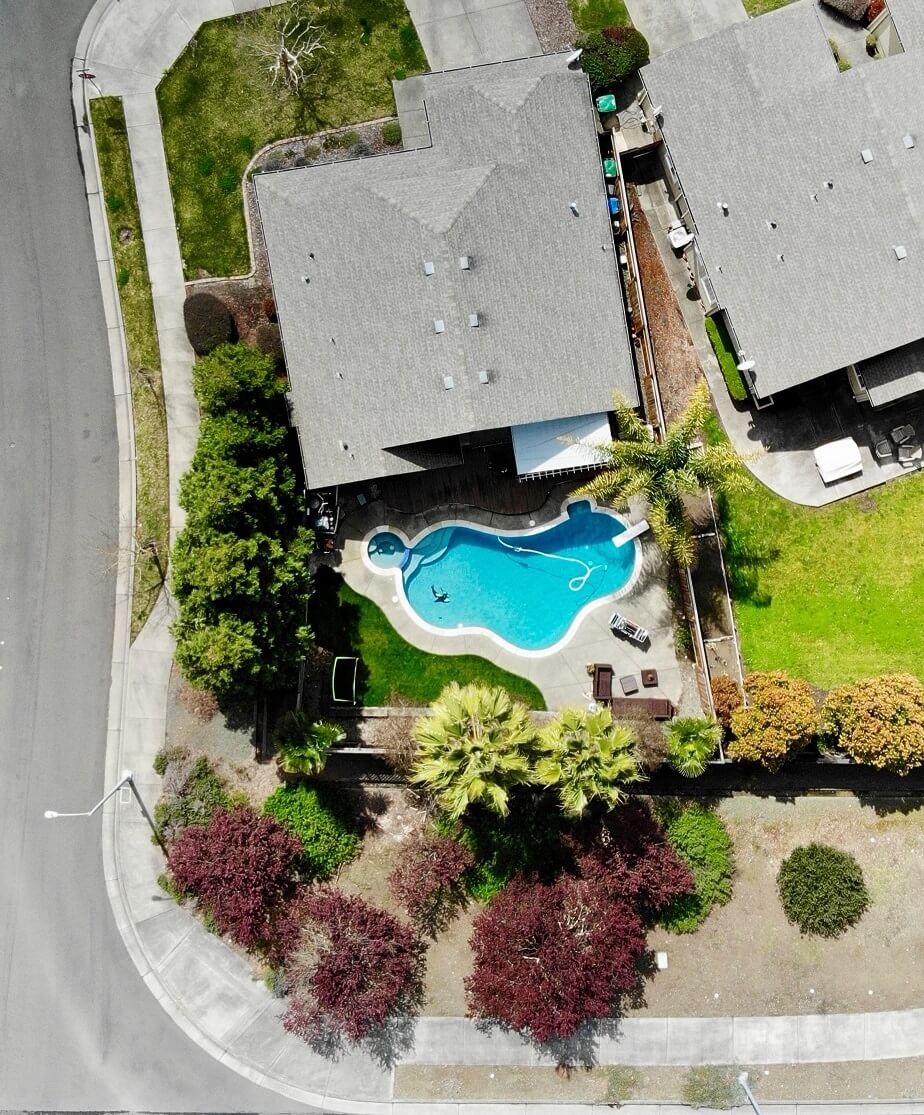 Aerial view of a home and backyard with a large pool and tropical trees.