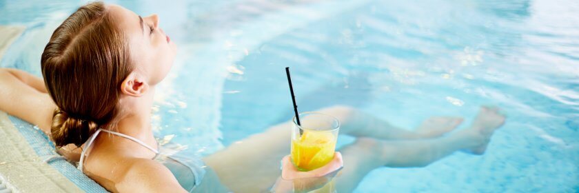 A woman enjoying a relaxing soak in a custom spa, drink in hand.