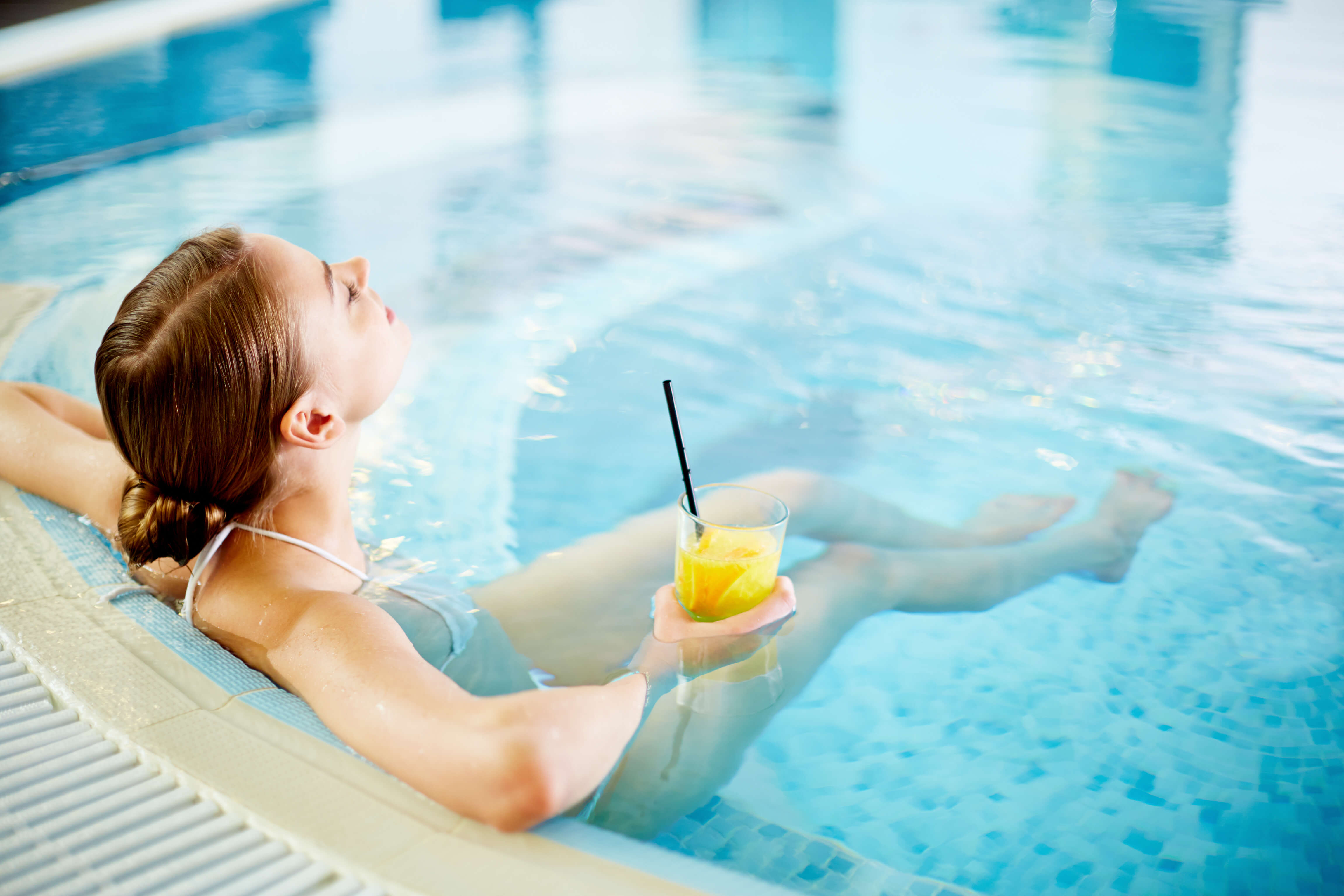 A woman enjoying a relaxing soak in a custom spa, drink in hand.