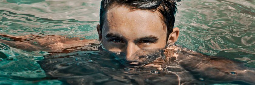 A young man floats in a saltwater pool, with just his eyes and forehead above the water line.