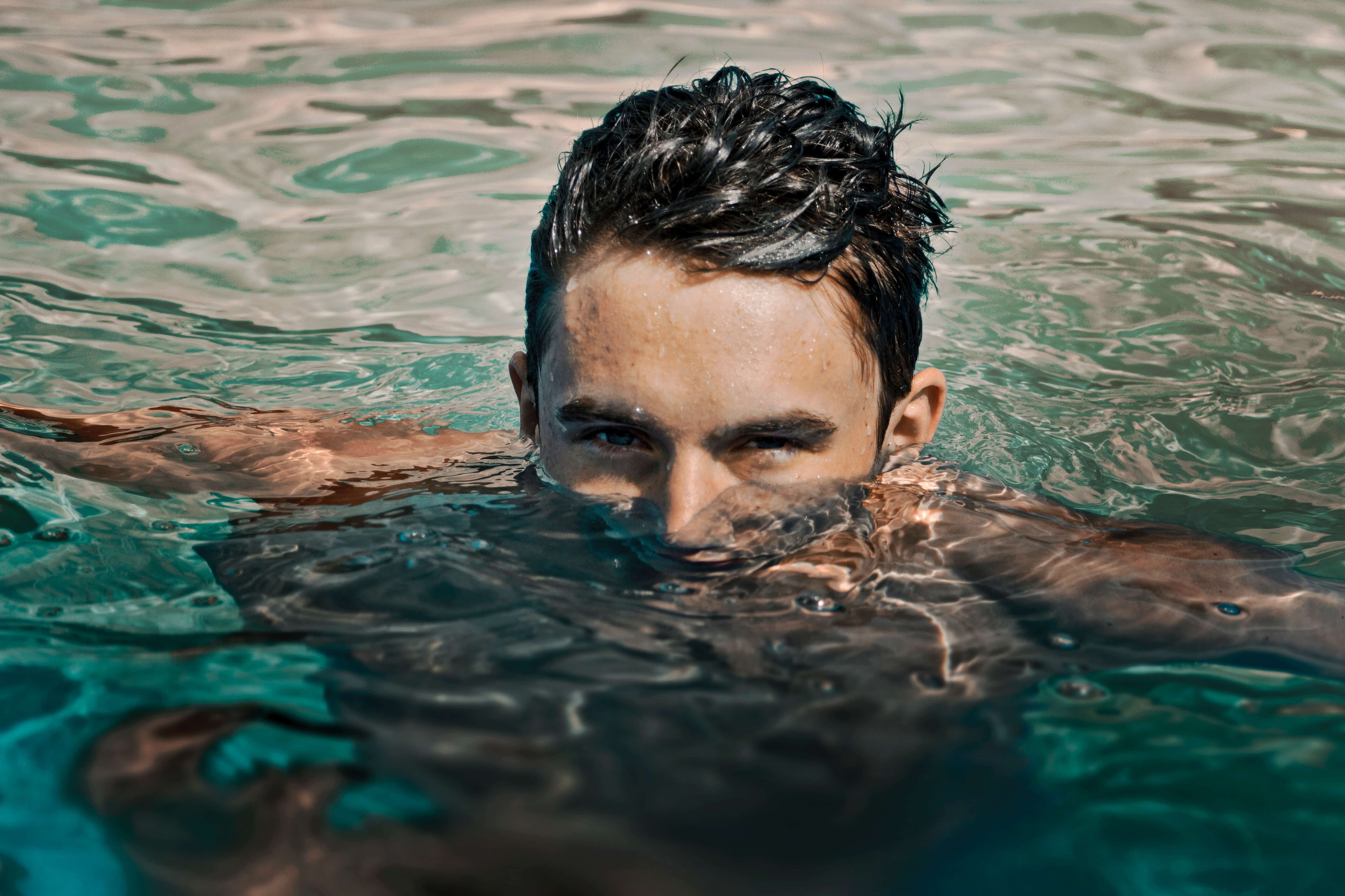 A young man floats in a saltwater pool, with just his eyes and forehead above the water line.