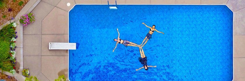 Three people perform hydrotherapy techniques in their inground backyard swimming pool.