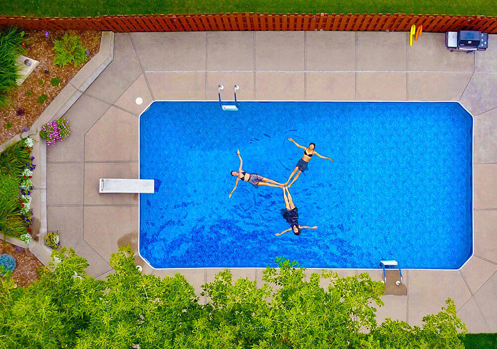 Three people perform hydrotherapy techniques in their inground backyard swimming pool.