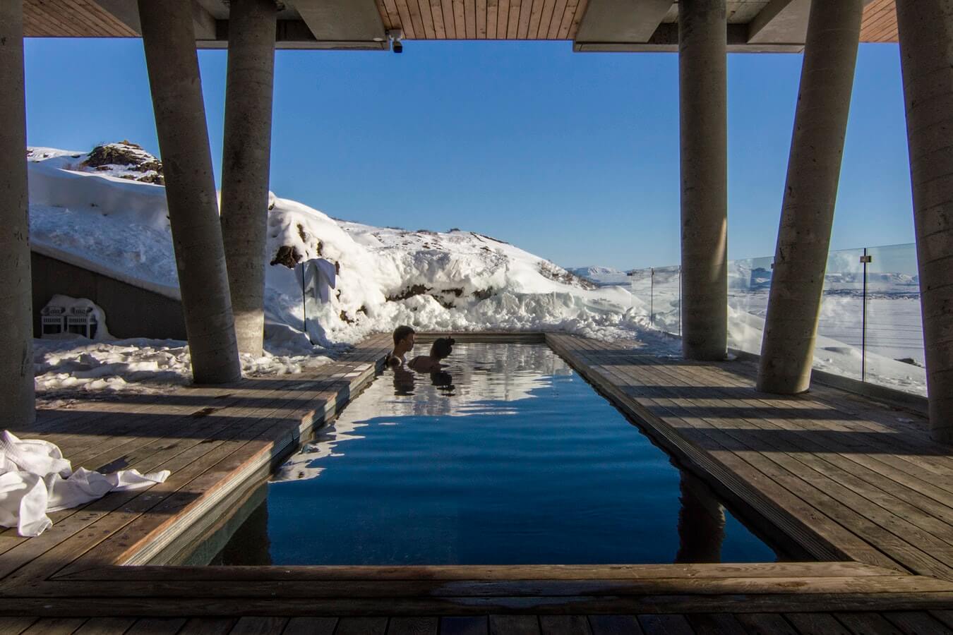 A couple sit in a a heated inground pool in the middle of winter.