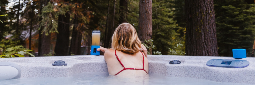 Woman wearing red bikini drinking a beverage leans over hot tub looking at trees in winter
