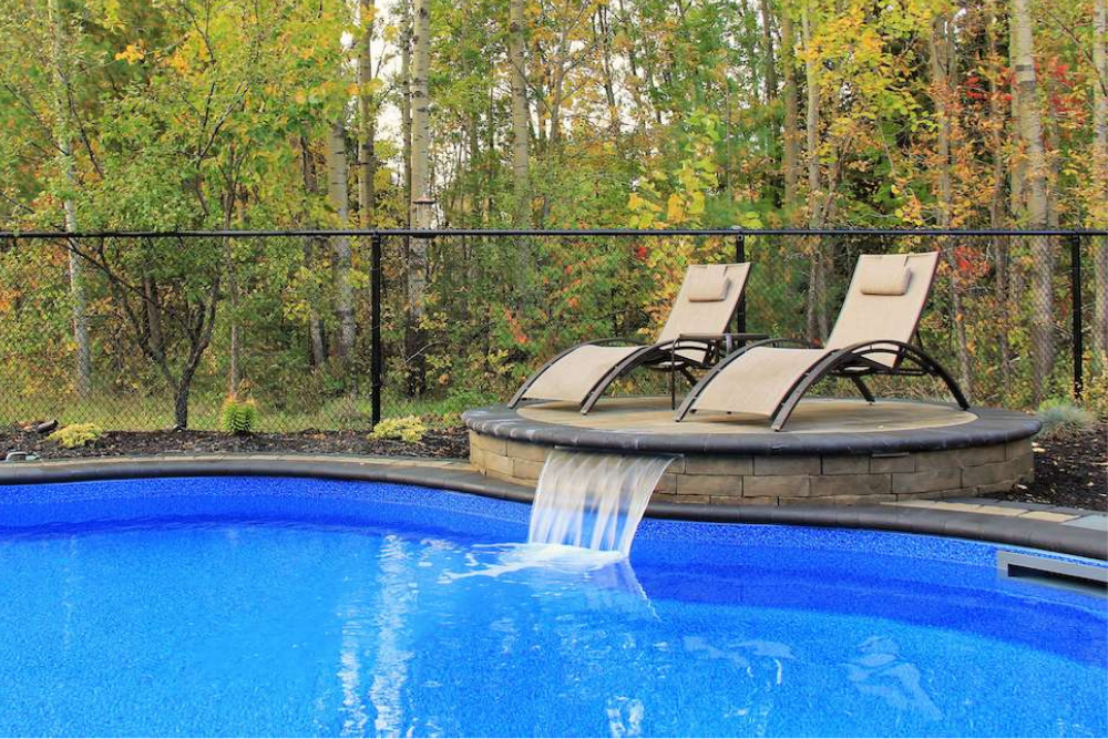 inground pool with spa and deck chairs enclosed by a fence