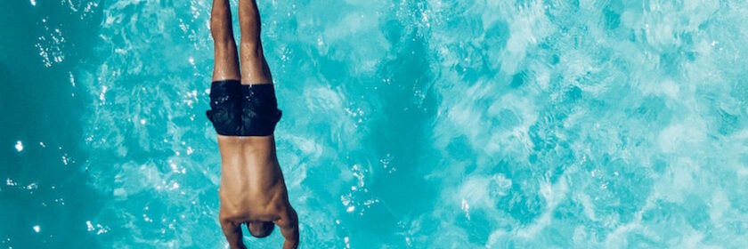 Man in blue bathing suit diving into a swimming pool