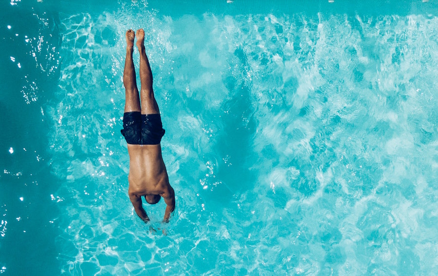 Man in blue bathing suit diving into a swimming pool